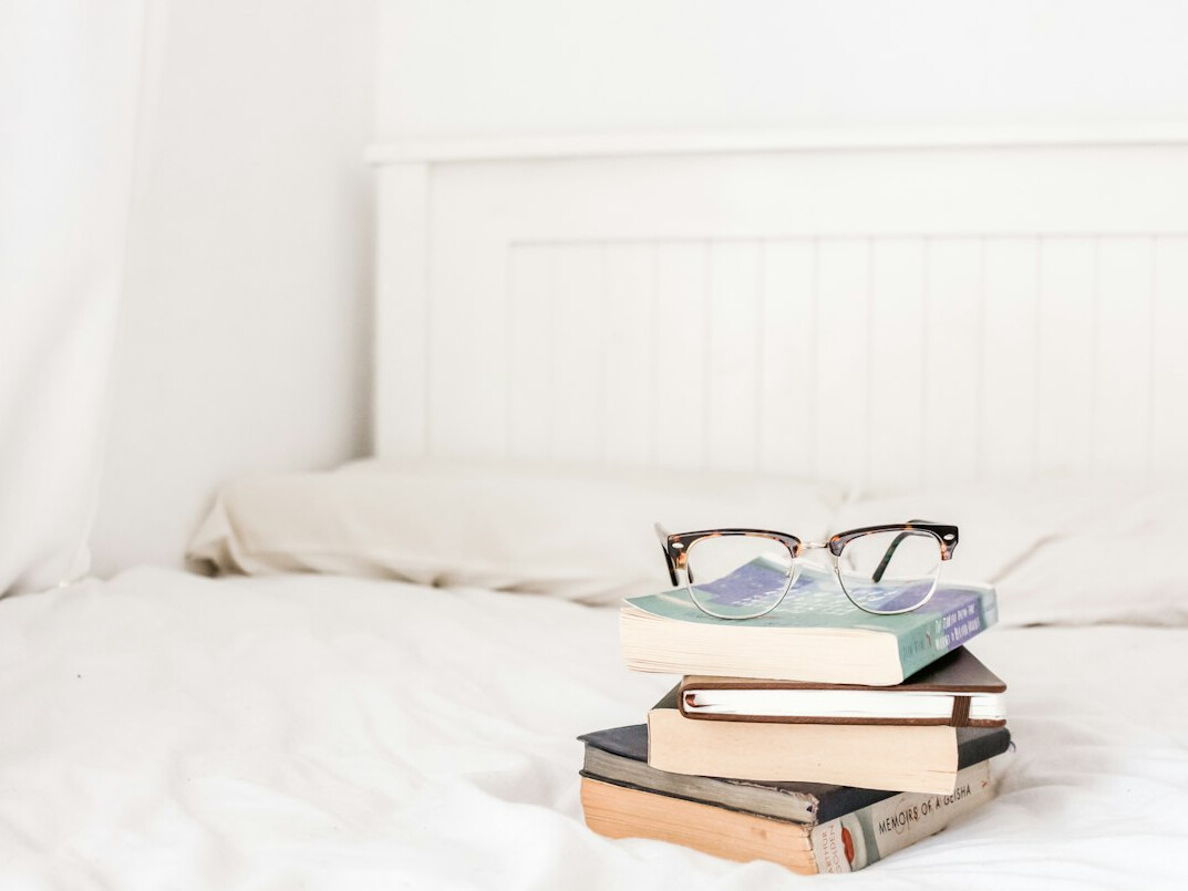 Stacked books with reading glasses on top in soft light